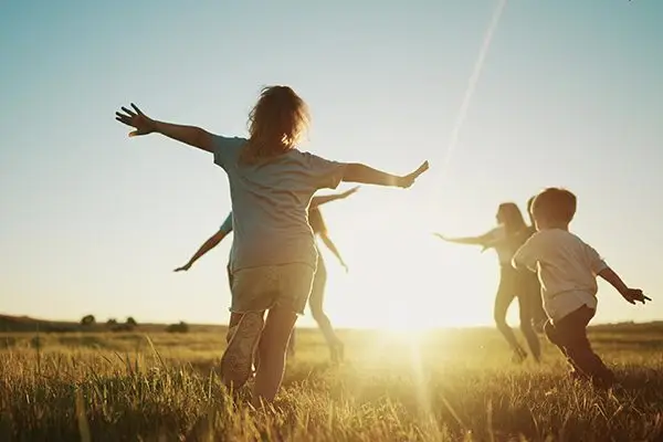 Children running and playing in a grassy field at sunset with arms outstretched.