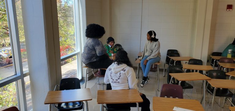 Four Year Two participants talking in a sunlit classroom, with empty desks and large windows in the background.