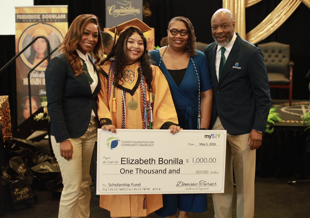 Four people smile as a graduate holds a 1,000 scholarship check with her name on it at an award event.