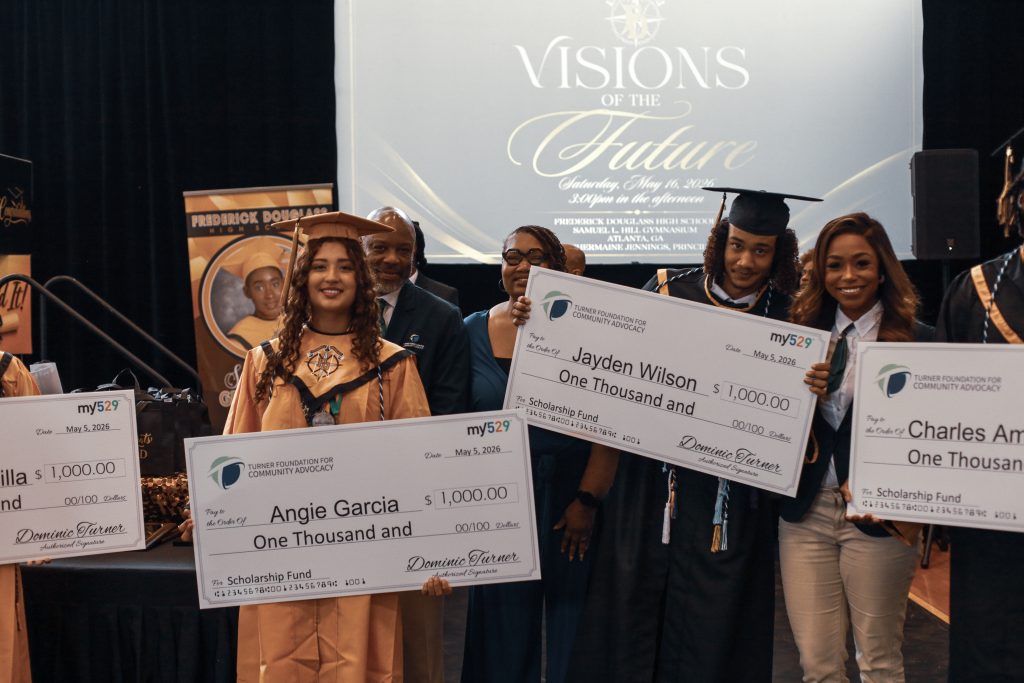 Graduates in caps and gowns hold large scholarship checks on stage at an award ceremony.
