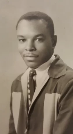 Black-and-white portrait of a young man in a suit and polka dot tie, looking at the camera.