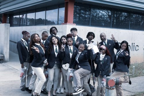 A group of students in uniforms pose playfully for a photo outside a modern building.