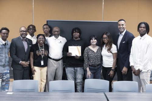 A group of people poses together indoors, one person in the center holds a certificate and smiles.