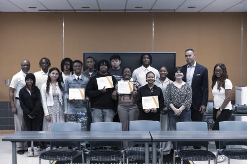 A group of people pose indoors, with several holding certificates and smiling at the camera.