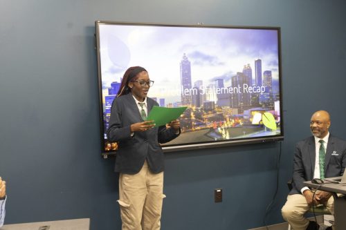 Person presenting with green paper in front of a screen displaying Problem Statement Recap in an office.